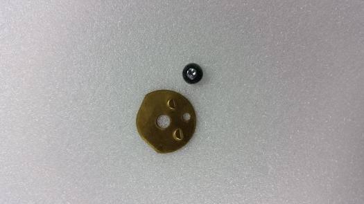 Gold-colored model kit gear with holes and small black bearing on white surface