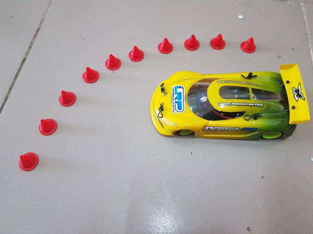 Yellow and green RC race car with red cones on tiled floor, ideal for hobbyists and collectors